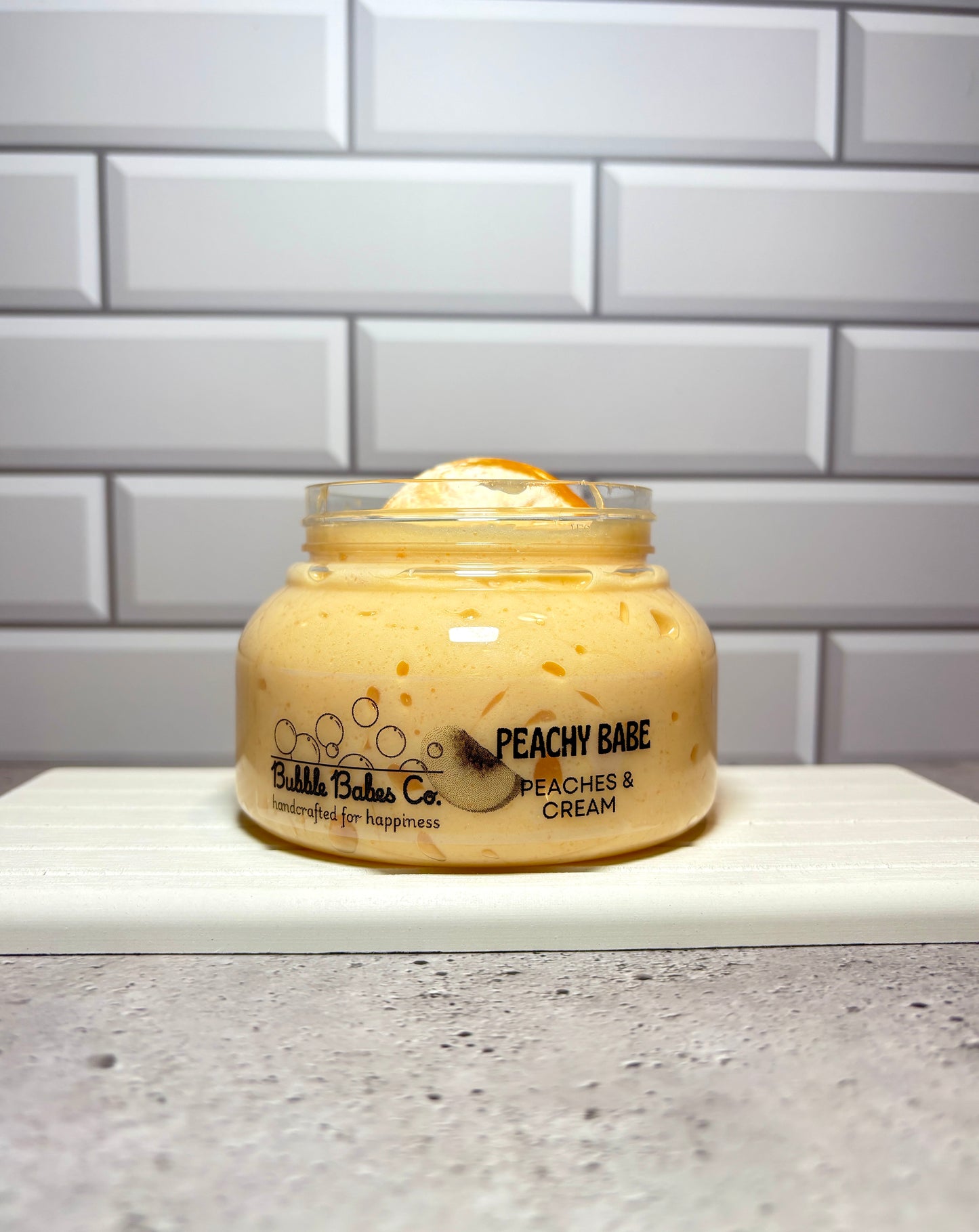 Jar of 'Peachy Babe' cream on a countertop with a tiled wall background